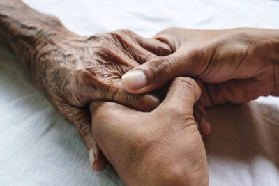 Adult's hands hold senior's hand tightly